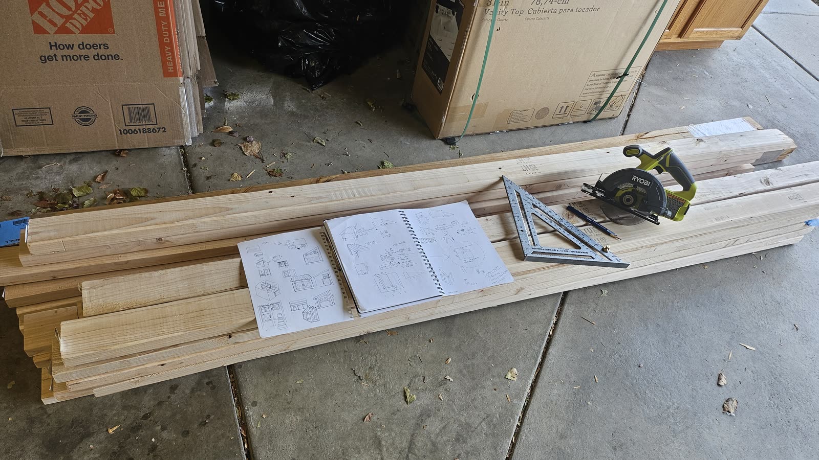 Fresh lumber stacked on the driveway with the sketchbook, a speed square and a circular saw on top.