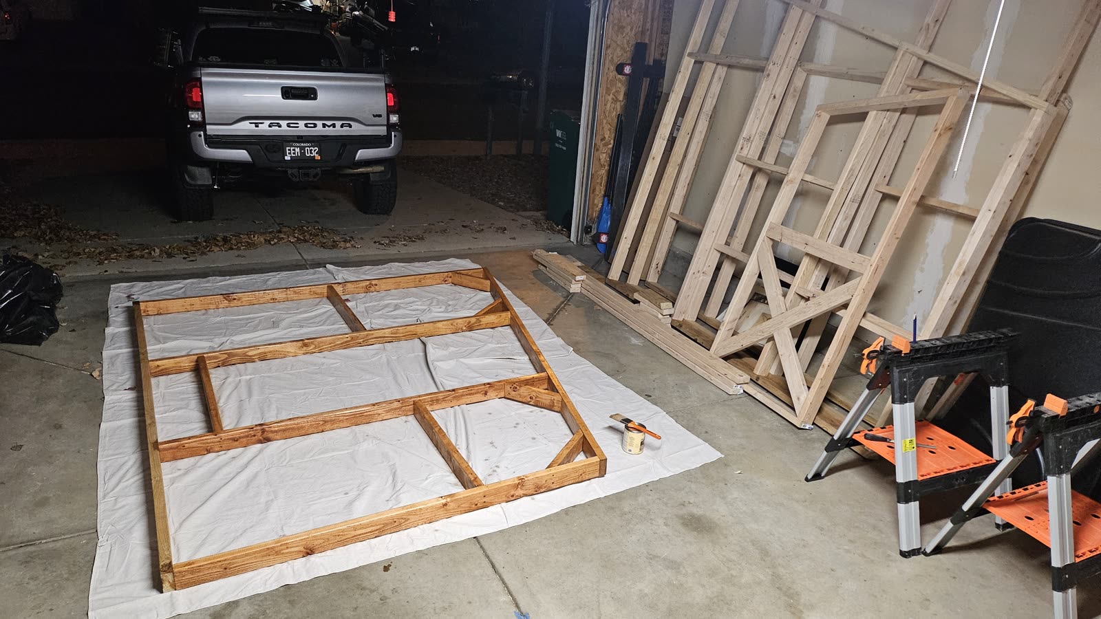 A wall frame laid out flat on a drop cloth in the driveway for staining.